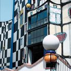 Kalenderblatt mit Januar 2027. Gebäude mit bunten, geometrischen Mustern und unregelmäßiger Fassade.