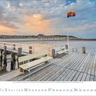 Kalender unten: Januar 2023, Wochenbeginn Montag. Steg mit Bank, Meer, schaukelnde Flagge, bewölkter Himmel bei Sonnenuntergang.