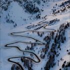 Kalenderseite im Januar 2027. Verschneite Serpentinenstraße in alpiner Landschaft mit bewölktem Himmel in der Dämmerung.