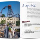 Ein hoher Looping einer Achterbahn über einem Gebäude. Links Essbereich mit Tischen und Stühlen, Palmen und blauer Himmel.