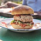 Es gibt keinen erkennbaren Text. Ein Burger mit Sesambrötchen, Salat und Tomatenscheiben auf einem Teller im Freien.