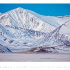 Januar 01-31: Schneebedeckte Berge unter blauem Himmel, karge Landschaft im Vordergrund.