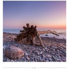 01. Drammatischer Sonnenuntergang am steinigen Strand mit großem Treibholz, strahlt Ruhe und Gelassenheit aus.