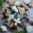 Papierornamente in verschiedenen Farben und Formen liegen auf einem Holzteller, umgeben von grünem Blattwerk.