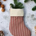 Gestreifter Weihnachtssocken mit Tannenzweig darin, umgeben von Walnüssen und Tannenzapfen auf betonähnlichem Hintergrund.