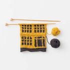 Strickmuster aus gelber und schwarzer Wolle auf Stricknadeln, mit zwei Wollknäueln daneben.