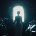 Eine Person mit Krone steht in einer dunklen Höhle vor einem hellen Ausgang, Silhouette beleuchtet.