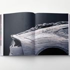 Keine Texte erkennbar. Abbildung eines modellierten Fahrzeughecks, umgeben von Tüchern, in einem aufgeschlagenen Buch.