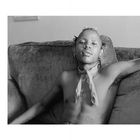 Es gibt keinen sichtbaren Text im Bild. Eine Person sitzt lässig auf einem Sofa, mit Piercings und einem Halstuch.