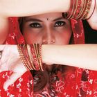 Ich kann die Person nicht identifizieren, aber sie hat rot-goldene Armreifen und trägt ein rotes, mit Blumenmuster verziertes Tuch.