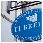 Blaues Schild mit dem Text: "CRÊPERIE BRETONNE TI BREIZ - HAUS DER BRETAGNE", dazu eine einfache Hauszeichnung.