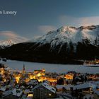 Text "Mountain Luxury". Nachtaufnahme einer beleuchteten Stadt vor schneebedeckten Bergen.
