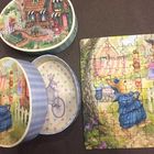 Auf einer Schachtel steht "R&D". Zu sehen sind ein Puzzle und dessen Verpackung, mit einem Hasen in einem Dorf.