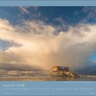 Januar 2027 Kalender, Nationalpark Wattenmeer. Ein Pfahlbauhaus steht in einer stürmischen Meereslandschaft unter dramatischen Wolken.
