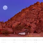 01. Ein weißes Auto mit Dachzelt steht vor einer felsigen Landschaft unter einem vollen Mond am klaren Nachthimmel.