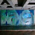 Graffiti: "STEPORE" neben einer runden Öffnung. Bunte, abstrakte Malerei in Blau- und Grüntönen auf einer Betonwand.