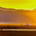 Keine Texte sichtbar. Landschaft in warmen Gelbtönen, Berge im Hintergrund, Jurte in der Ebene, Sonnenuntergangsstimmung.