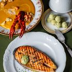 Gegrilltes Lachssteak mit Kräuterbutter, Hummerbisque mit Hummerstücken, Kräuterbutterkugeln auf edlem Porzellan.