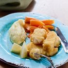 Ein türkisfarbener Teller mit Fischstäbchen, Kartoffelpüree, Möhren und Zitronenscheiben. Daneben liegt Besteck.