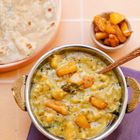 Ein Teller mit gelbem Linsen-Curry, garniert mit Kürbisstücken, daneben Fladenbrot und ein kleines Schälchen Pickles.