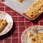 Kein Text ersichtlich. Ein rechteckiger Streuselkuchen auf Backblech, daneben Teller mit Stücken, Gabel auf einem Teller.