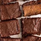 Dicht aneinander liegende Brownie-Stücke mit glänzendem Schokoladenüberzug, eines zeigt die weiche Innenseite.