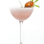 Ein Cocktailglas mit rosa Getränk, garniert mit einer getrockneten Limettenscheibe und Rosmarinzweigen.