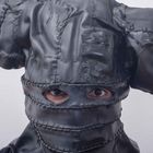 Person trägt eine Maske aus zusammengenähtem, schwarzem Material; Augen schauen durch Schlitze hervor.