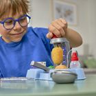 Ein Kind mit blauer Brille und blauem Shirt spielt konzentriert mit einer Spielzeugmaschine und Knete.