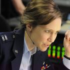 Eine Frau in einer US-Militäruniform spricht in ein Headset; im Hintergrund sind bunte Lichter zu sehen.