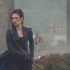 Eine Frau in blauer Kleidung hält ein Schwert. Im Hintergrund sind Soldaten und eine britische Flagge im Nebel zu sehen.