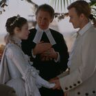 Ein Paar in historischen Gewändern hält Hände, während ein Geistlicher sie traut. Deko aus Blättern im Hintergrund.