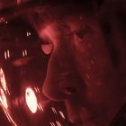 Kein Text vorhanden. Eine Nahaufnahme eines Gesichts in einem Helm, rötlich beleuchtet, wofür ein Space-Setting vermutet wird.