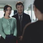 Zwei Personen schauen ernst auf eine unsichtbare Person. Die Frau trägt eine grüne Strickjacke, der Mann einen Anzug.