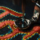 Der Buchstabe "T" ist in Rot auf dunkelblauem Stoff gestickt, von einer Nähmaschine bearbeitet.