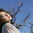Keine erkennbaren Texte. Eine Frau mit geschlossenen Augen vor einem blauen Himmel und kahlen Ästen.