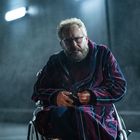 Ein Mann mit Bart in einem Rollstuhl trägt einen gestreiften Bademantel. Die Szene ist neblig und düster beleuchtet.