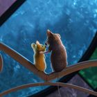 Zwei niedliche Mäuse sitzen vor einem bunten Fenster mit blau, grün und rosa Teilen auf einem geschwungenen Geländer.