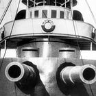 „In Erinnerung“ ist auf einem Schiffsaufbau zu sehen, darunter zwei Kanonen und zahlreiche Drahtseile.