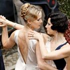 Zwei elegant gekleidete Frauen tanzen eng umschlungen miteinander. Eine trägt ein weißes, die andere ein cremefarbenes Kleid.