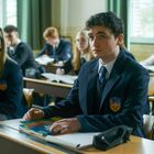 Ein Klassenzimmer mit Schülern in Uniformen, die aufmerksam dem Unterricht folgen. Im Vordergrund sitzt ein Junge.
