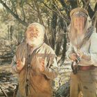 FSK-Zeichen unten rechts. Ein älterer Mann mit Bart und Kopftuch, flehend. Ein Mann mit Gewehr und Hut mit Netz.