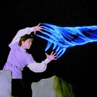 Ein Mann in violetter Kleidung wirft magische blaue Energie in die Luft bei Nacht.