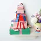 Rechteckige Geschenke mit blauen und roten Schleifen, bunte Blumen in Vase mit Gesichtsmotiv.