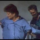 Zwei Männer, einer in blauem Hemd und der andere in kariertem, kämpfen miteinander in einem Raum. Sie wirken angespannt.