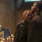 Worte an der Wand: "PURITY," "DEATH," und "JUSTICE." Zwei Personen umarmen sich vor einem Altar mit Fotos und Kerzen.