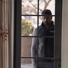 Auf Jacke: "Great Pines Landscapes". Ein Mann steht ernst hinter einer Glastür, umgeben von innenliegenden Pflanzen.