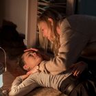 Zwei Personen, eine liegend am Boden und eine kniend, berührt sie fürsorglich. Eine Laterne erhellt die Szene.