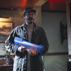 Text: "PSYCHO HYDRO". Ein Mann mit Brille und Mütze hält ein großes blau-orangefarbenes Spielzeuggewehr.