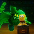 Grüner Pirat erhellt den Raum, umarmt einen gelben Schwammcharakter, beide auf einer Holzkiste in einem Raum voller Gegenstände.